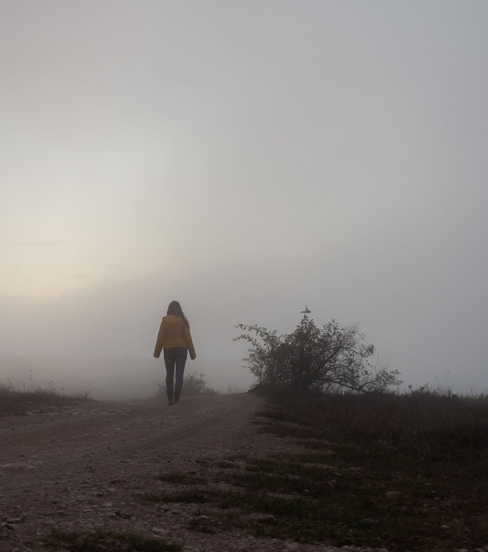young woman walking on a foggy path with a yellow jacket